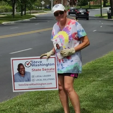 A volunteer holding a Steve Washington for State Senate sign by the roadside